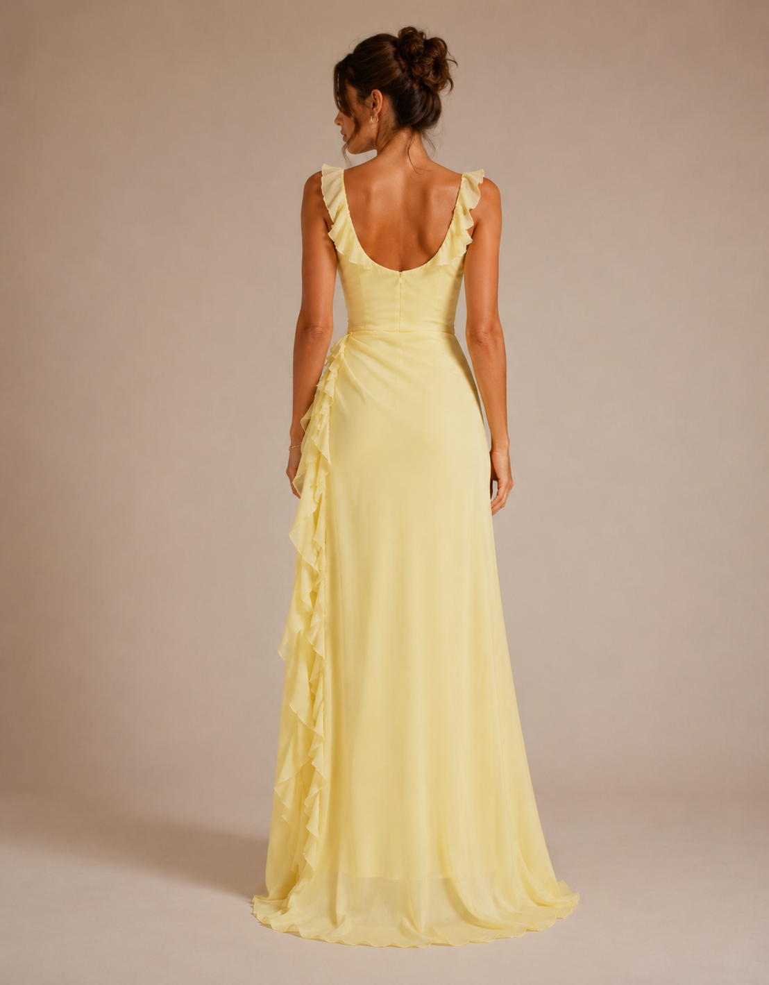 A woman modeling a pale yellow sleeveless maxi dress from the back, featuring ruffled shoulder straps, a deep V-neckline, and cascading ruffles down the side, set against a solid beige studio background.